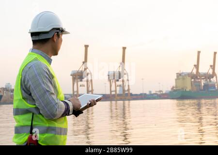 Engineering is using the tablet. To check the details and use in the work order for flexibility Cargo handling. The background is the shipping port. Stock Photo