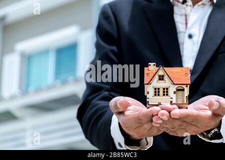 Home buying and selling agents. A businessman wearing a suit with a model house placed on his hand. Housing demand concept. Stock Photo
