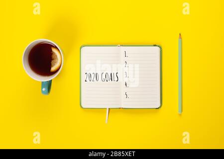 2020 goals banner. Notebook, pencil and cup of tea on a yellow background. Copy space, Flat lay. Stock Photo