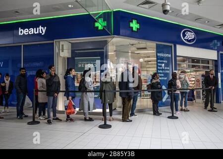 Wimbledon, London, UK. 20th Mar 2020. Customers queue outside Boots Pharmacy in Wimbledon, London, UK. 20th Mar, 2020. Families queuing to buy over counter medicines and essentials worried about the impact of the ‘UK Coronavirus Lockdown' looms. Contingency plans are to be put in place across the UK to ensure pharmacies remain open at this key time. Credit: Jeff Gilbert/Alamy Live News Stock Photo