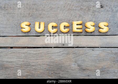 Put cookies into words that are success, Comparable to doing things that are difficult to see easily. Background is a wooden table.