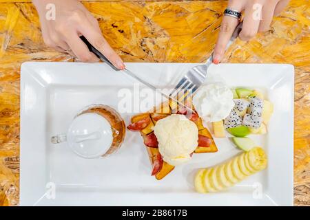 The woman's hand holding a knife and fork In order to eat Honey Santos of the cold that she likes. Ice cream that is placed on bread and contains bana Stock Photo