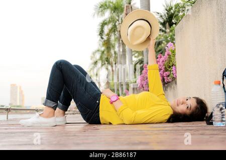 Women who are sleeping in the park happily on wooden floor patio. Wearing a yellow shirt, jeans, white sneakers, a water bottle placed on the side. Sh Stock Photo