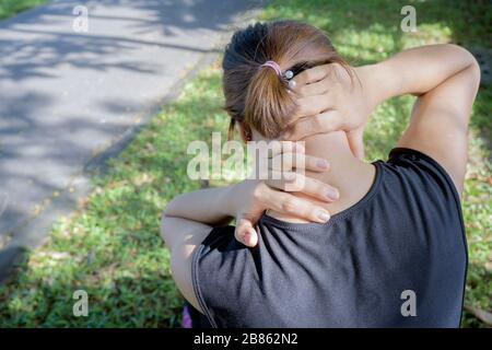 Neck pain during training. woman runner with sport injury in sports bra rubbing and touching upper back muscles outside after exercise workout in summ Stock Photo