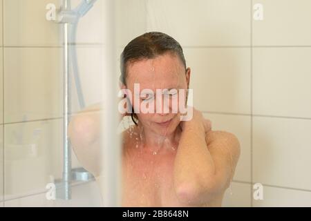 Woman enjoying a hot shower rinsing her hair after shampooing it under the running water in close up in a personal hygiene concept Stock Photo