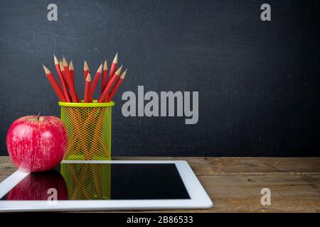 Concept back to school to get an education, learn, tablet, apple red, red pencil, on the table. The background is a blackboard with text and pictures. Stock Photo