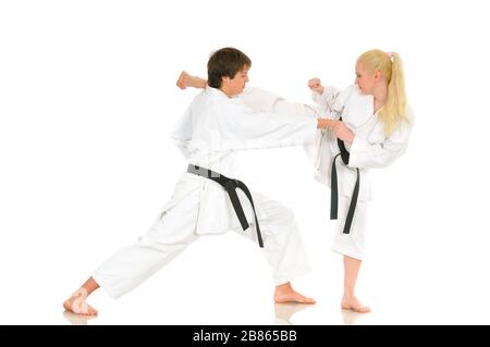 Cute blonde girl and a young cheeky guy karate are engaged in training in a kimono on a white background. Young couple of athletes getting ready for a Stock Photo