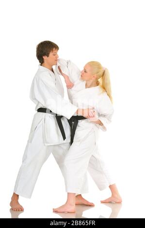 Cute blonde girl and a young cheeky guy karate are engaged in training in a kimono on a white background. Young couple of athletes getting ready for a Stock Photo