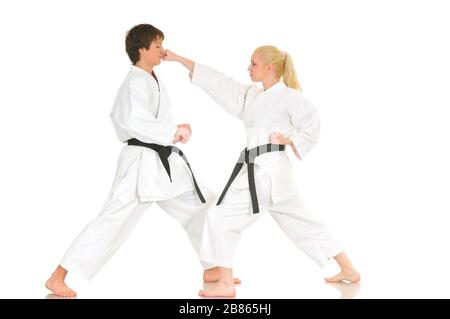 Cute blonde girl and a young cheeky guy karate are engaged in training in a kimono on a white background. Young couple of athletes getting ready for a Stock Photo