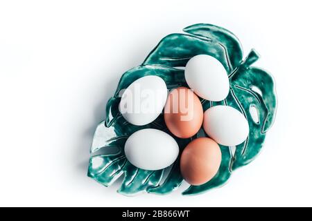 Several chicken eggs lie on a ceramic plate in the form of a tropical leaf on white background Stock Photo