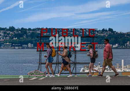 Tourists Walking Down First Avenue in Seattle with Public Market sign in Backyard Stock Photo