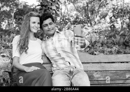 Happy multi ethnic couple smiling while taking selfie together at the park Stock Photo