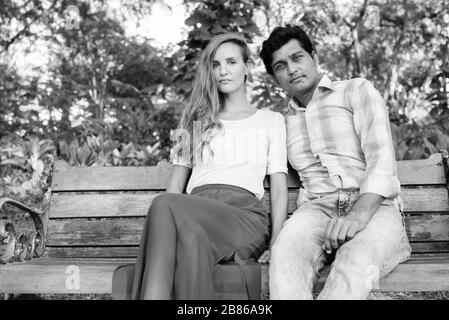 Multi ethnic couple sitting on wooden bench in love at the park Stock Photo