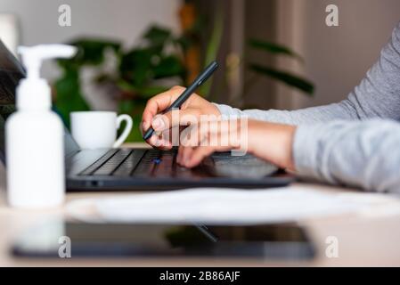 close up of hands of young woman typing on laptop keyboard with hand sanitizer while remote working due to corona virus spread Stock Photo