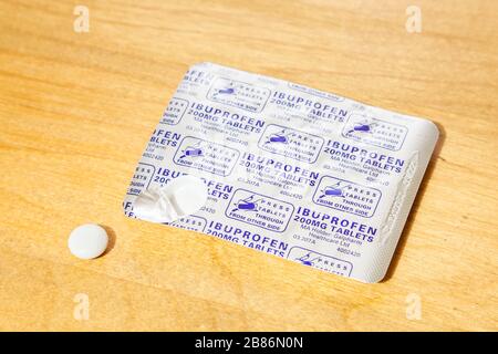 Pain relief pills. Ibuprofen 200mg tablets in a blister pack with one tablet removed from the packet and placed on a wooden table Stock Photo