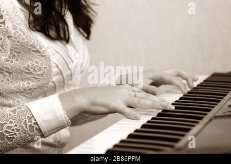 Female hands on piano. Brunette woman in white blouse playing musical composition. Gold ring on finger Stock Photo