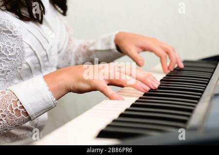 Female hands on piano. Brunette woman in white blouse playing musical composition. Gold ring on finger Stock Photo