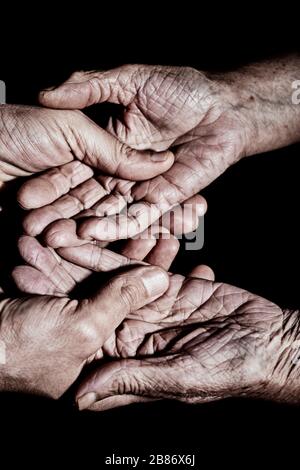 closeup of a young caucasian man holding the hands of an old caucasian woman with affection, with a dramatic light Stock Photo