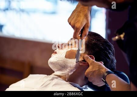 Shaving process of beards in Barbershop. Master makes the client shave his beard with vintage straight razor. Work in the Barber shop, The process of Stock Photo