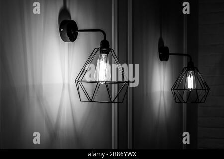 Black and white stock photo of modern pendant light in diamond shape wire lampshade with light bulb inside. Glowing filament in lamps of minimal style Stock Photo