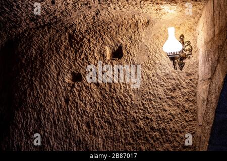 Ancient rough wall in cave with light from lamp in darkness. Antique lamp on scratched surface of natural limestone wall in cave of Cappadocia Turkey Stock Photo