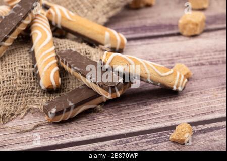 Cookie sticks with white icing and chocolate and pieces of brown cane sugar on a wooden background. Close up Stock Photo