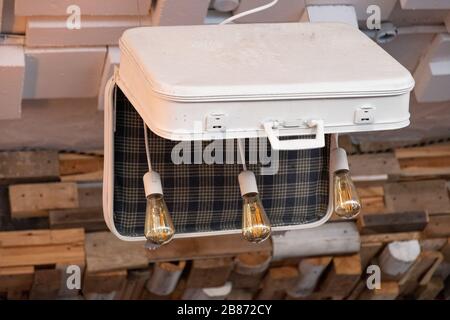 Unusual chandelier made from old suitcase with three Edison glass lightbulbs inside. White suitcase retro style with plaid pattern inside. Retro style Stock Photo