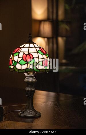 https://l450v.alamy.com/450v/2b873ak/stained-glass-lampshade-with-floral-pattern-closeup-on-dark-blurred-background-shiny-mosaic-lamp-atop-wooden-table-surface-vintage-ornate-lamp-shade-2b873ak.jpg