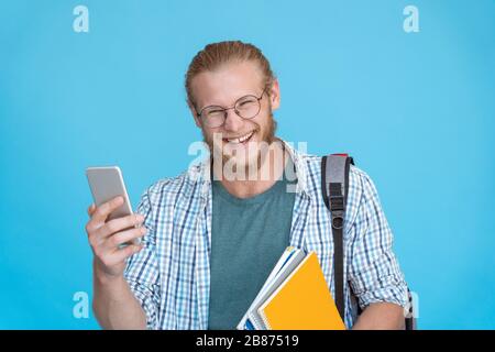 Cheerful man student laughing hold phone isolated on blue background. Stock Photo