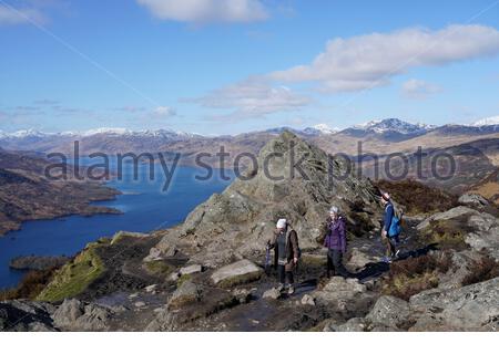 Trossachs, Scotland, UK. 20th Mar 2020. Hikers on the summit of Ben A'an looking down towards Loch Katrine and snow capped mountains on a clear sunny day. Credit: Craig Brown/Alamy Live News Stock Photo