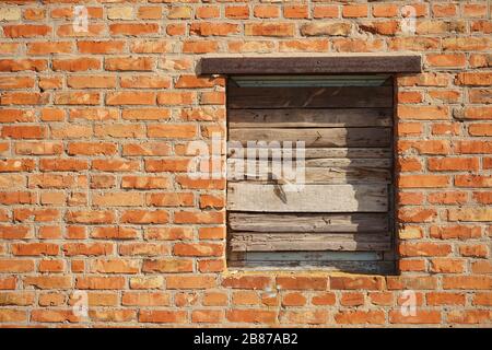 Boarded up with wooden planks window opening in an old red brick wall. Afternoon Lighting Stock Photo