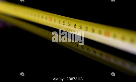 A yellow graduated meter resting on a shiny black surface is reflected in it Stock Photo