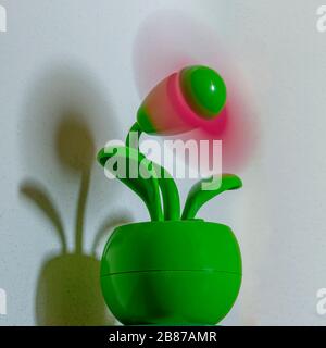 A nice colorful table fan in the shape of a flower pot with the moving blades and its shadow projected on the wall Stock Photo