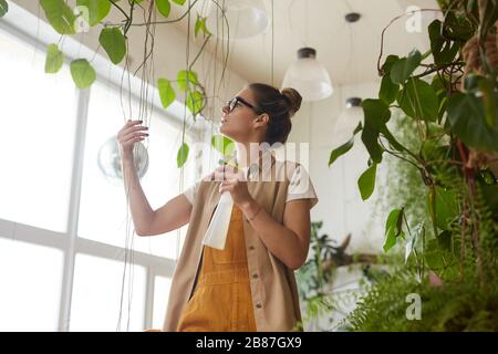Young woman watering plants from splashing bottle in the garden Stock Photo