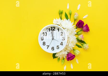 Alarm clock with small burgundy red roses, white peonies and petals isolated on yellow background. Flat lay, Top view. Selective focus, horizontal ima Stock Photo
