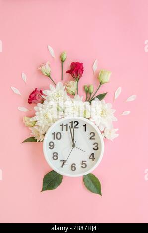 Alarm clock with small burgundy red roses, white peonies and petals isolated on pink background. Flat lay, Top view. Selective focus, vertical image Stock Photo