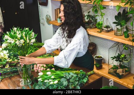 Attractive young woman florist is working in a flower shop.