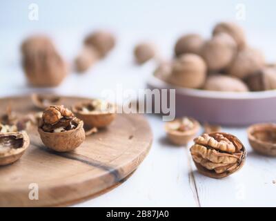 Walnuts kernels on a woody cutting board on white kitchen table desk as a background, Whole greek walnut in a wood vintage bowl. Selective focus Stock Photo