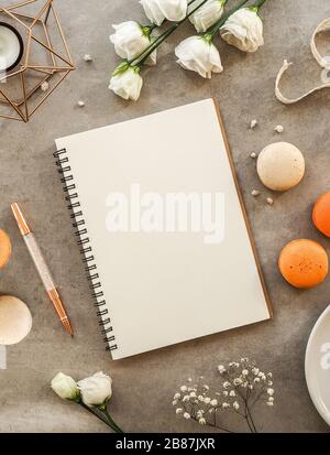 French orange and beige macaroon cakes, white gypsophilas and roses flowers, pen and notebook for recipes flowers on gray stone background. Flat lay, Stock Photo