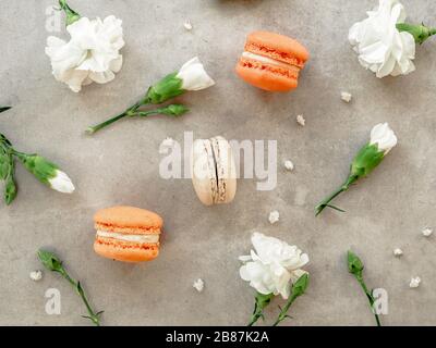 French orange and beige macaroon cakes and white chrysanthemums flowers on gray stone background. Flat lay, top view. Selective focus. Stock Photo