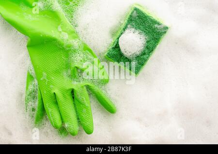 Top view of protective green gloves and sponge on soapy background. Housework concept. Copy space, top view Stock Photo
