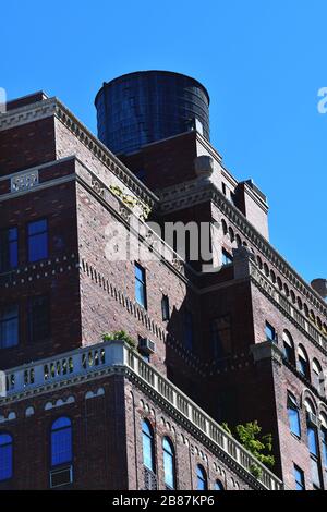 New York City, USA-September 2019; Low angle view of the brown brick building with its ornaments with a wooden water tower on the roof against a blue Stock Photo