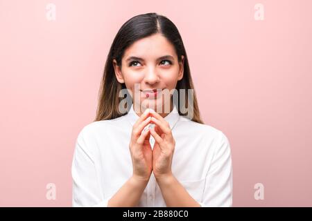 young sneaky woman, scheming something for april first, fools day against pink background Stock Photo