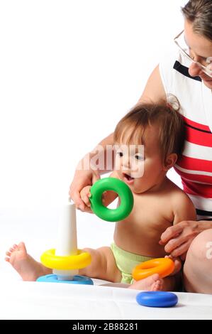 Interested child training play with pyramid. Little baby playing with parent and holding ring of toy. Portrait on isolated white background Stock Photo