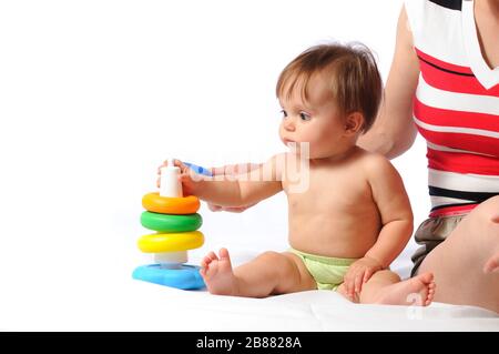 Interested child training play with pyramid. Little baby playing with parent and holding ring of toy. Portrait on isolated white background Stock Photo