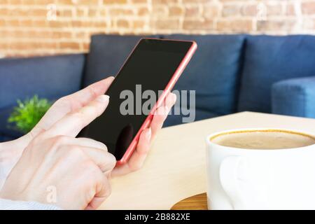 Woman hand using smartphone against home interior. Freelance or blogging concept. Coffee break. Stock Photo