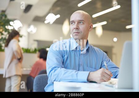 Portrait of smiling bald man looking away dreamily while working with laptop in office, copy space Stock Photo