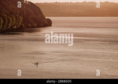 Man alone on Stand Up Paddle in the middle of the lake at sunset, enjoying nature while doing sport and meditation Stock Photo