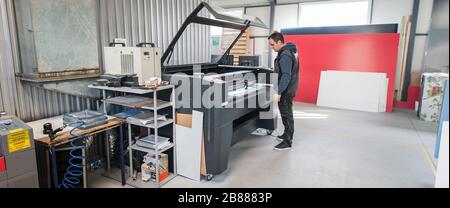 Printshop worker technician works on Laser CNC computer numerical control printing and cutting machine Stock Photo