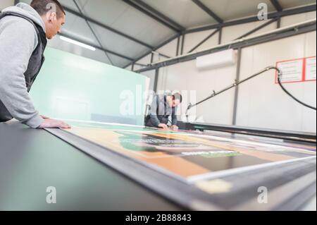 Two printshop worker technicians works on large CNC computer numerical control printing and cutting machine Stock Photo